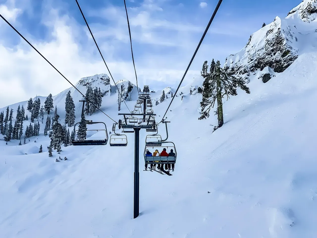 Blick entlang einer Sesselbahn über verschneite Piste, Fahrgäste von hinten auf einem Sessel